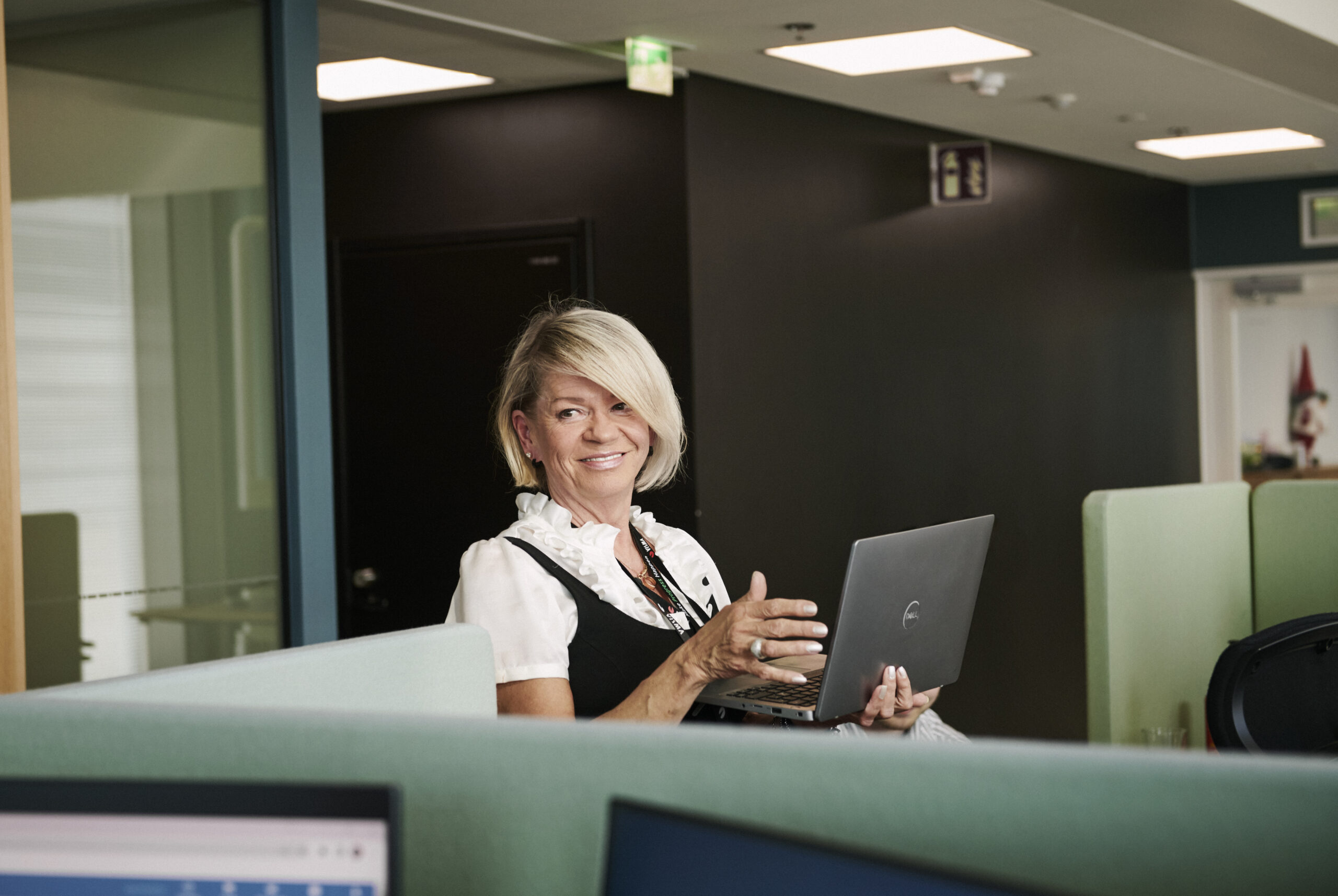 Hymyilevä nainen kannettavan tietokoneen kanssa toimistolla